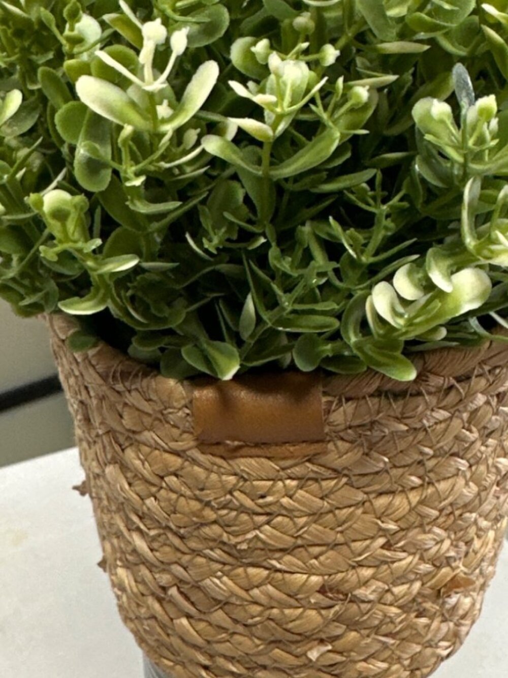 Planta artificial decorativa con follaje verde y pequeños detalles en color blan